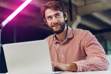 Portrait of young caucasian businessman using laptop computer at his workplace in modern office