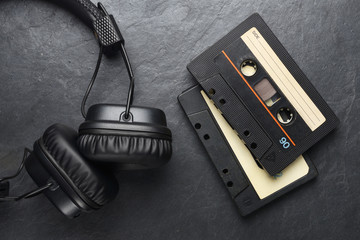 Headphones and compact cassettes on black slate background