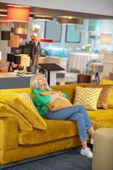 Obraz premium Blonde woman in a green blouse spending time in a furniture salon