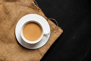 White cup of coffee and jute for grains on dark background