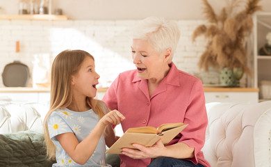 Excited granny and her granddaughter reading book together at home