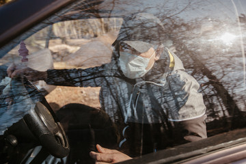 A man in a medical mask (respirator) gets out of a car during an epidemic