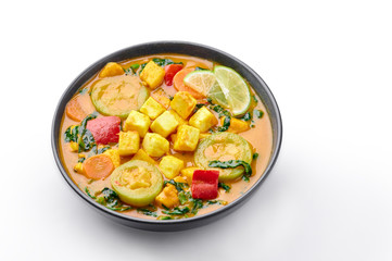 A Yellow Veg Thai Curry with Tofu and vegetables isolated on white background. Vegetarian Thai Curry with tofu, zucchini, bell pepper, spinach, carrot. Thai Food. Indian vegetable curry. Copy space