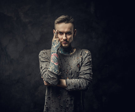 Young adult male model posing in a dark studio wearing ripped longsleeve jumper, tattooed in a japanese irezumi style, thinking pose with serious face expression