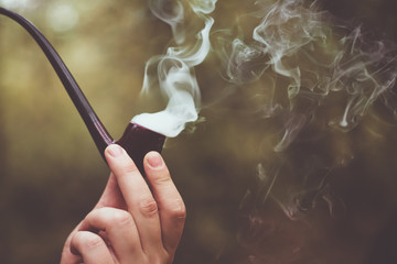 Close up smoking tobacco pipe on blurred background outdoor. Brown toned photo