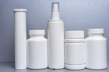 5 white jars for medicines and vitamins and dietary supplements without a name are on a gray shelf.