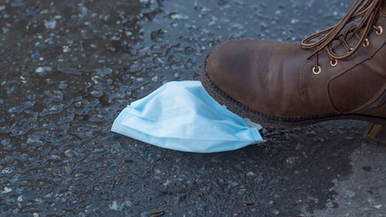 A protective medical face mask is lying on the muddy ground. Mask for protection from the flu epidemic, viruses and coronavirus.