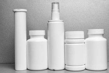 5 white vials without labels for medicines, vitamins, sprays, liquids are on a gray shelf. mockup for pharmacy and store design
