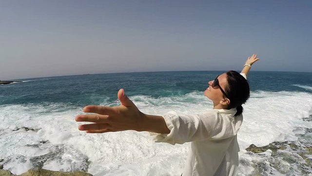 Slow motion footage woman standing on shore on clear sunny day raising hands. Summer holiday footage. Travel concept. Seaside holiday concept.
