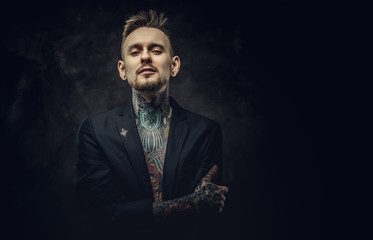 Seductive looking tattoo artist posing on a dark background wearing a black tuxedo on a half-naked...