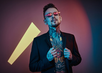 Grunge and cool male model holding a collar of his tuxedo in a neon studio, wearing fire-shaped...