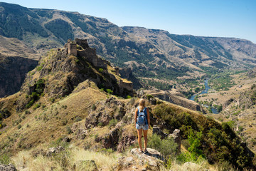 Woman tourist with backpack looking on fortress. Tmogvi, Georgia.