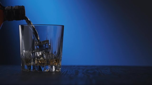 Close-up of glass of whisky with ice cubes. Whiskey poured in glass at blue background with copy space. Pouring skotch from bottle in slow motion