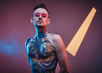 Self-assured male model posing in a neon studio with a half-naked body wearing fire-shaped...