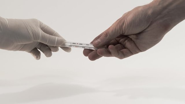 A nurse in medical gloves gives a sick thermometer to measure a person's body temperature close up. The doctor passes the thermometer to the patient.