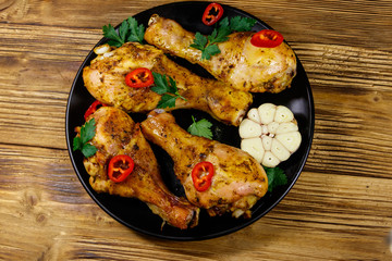 Roasted chicken drumsticks with spices in a black plate on a wooden table. Top view