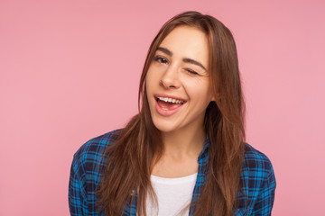 Fototapeta premium Closeup of coquettish happy girl in checkered shirt smiling and winking playfully, flirting to camera with optimistic expression, cheering you up. indoor studio shot isolated on pink background