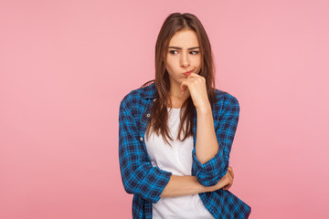 Portrait of thoughtful upset girl in checkered shirt pondering serious issues, looking with uncertain hesitant expression, making difficult choice. indoor studio shot isolated on pink background