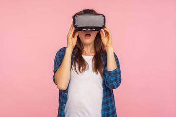 Portrait of amazed gamer girl in checkered shirt wearing vr headset, playing virtual reality game...