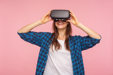 Portrait of happy gamer woman in checkered shirt wearing vr headset, playing virtual reality game with delighted smile, innovative computer technology. indoor studio shot isolated on pink background © khosrork