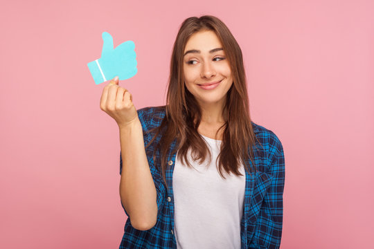 Portrait of attractive smiling girl in checkered shirt looking at blue thumb up icon, holding social media like button, recommending forums and blogs. indoor studio shot isolated on pink background - Powered by Adobe