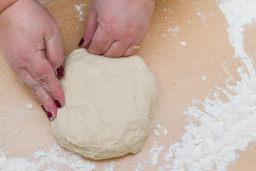 Kneading dough with flour on a wooden table at home