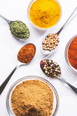 Variety of spices and herbs in spoons and bowls on white background, top view, vertical format. Cooking ingredients and condiments concept.