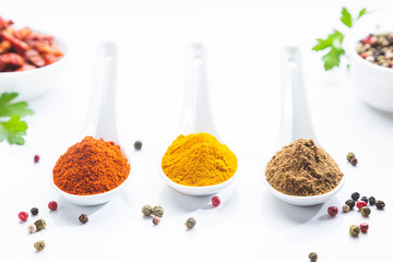 Three white spoons with paprika, turmeric and cumin on a white background. Cooking ingredients and...
