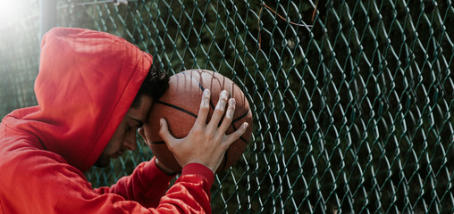 young teenage boy leaning on basketball ball outdoors