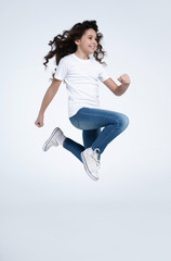 Excited and happy little brunette girl is jumping and shouting in white t-shirts and jeans isolated on white background.