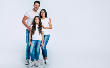 Happy beautiful young family in white t-shirts while they hugging each other isolated on a light background.