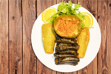 stuffed grape leaves, zucchini, and pepper, with rice and meat served in white plate with lemon and parsley. 