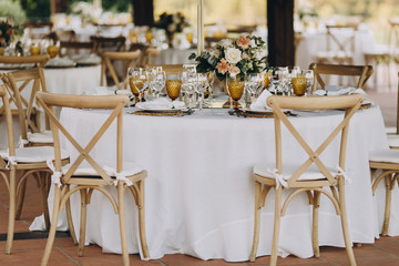 banquet tables are decorated with compositions of flowers and greenery, on the tables are plates with napkins, glasses, candles and name cards