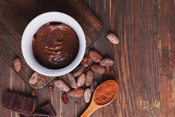Chocolate cream, cocoa beans and powder and pieces of chocolate on the wooden table