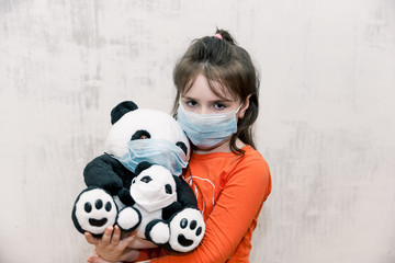 sad unhappy Little girl wearing protective mask with panda toy in her hands wearing medical mask on...