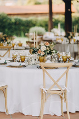 banquet tables are decorated with compositions of flowers and greenery, on the tables are plates with napkins, glasses, candles and name cards