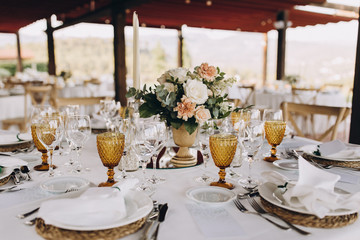 banquet tables are decorated with compositions of flowers and greenery, on the tables are plates with napkins, glasses, candles and name cards