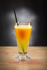 Fresh orange juice in glass with black straw on wooden background.