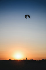 Silhouette of a kite in the sky, silhouette of a parachute, a man controls a parachute at sunset