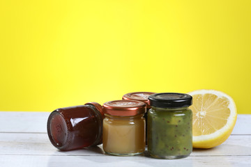 Jar of jam, honey, lemon on a wooden table, yellow background