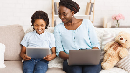 Afro mom and daughter using laptop and tablet