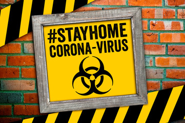 Sign in front of a clinker wall with stay home and corona virus