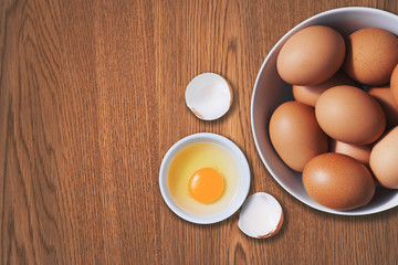 Chicken eggs with egg yolk in a bowl on wood table top view. Copy space is provided.
