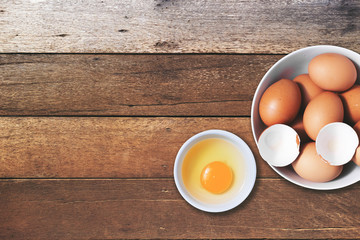 Top view of chicken eggs with egg yolk in a bowl on wood table. Copy space is provided.