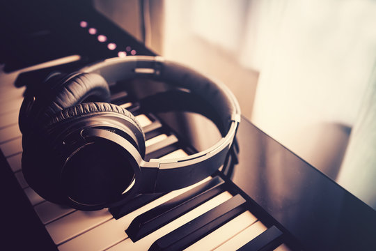 Black bluetooth headphone on piano keyboard with sunlight through the window. Vintage filter. Music and work from home concept.