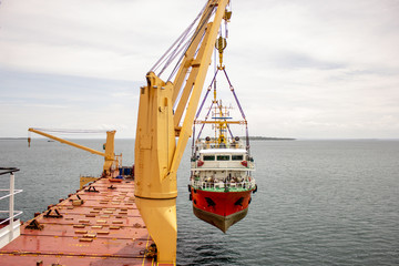a scientific ship is loaded onto a deck of a heavy lift vessel  by tandem of two cranes with a...