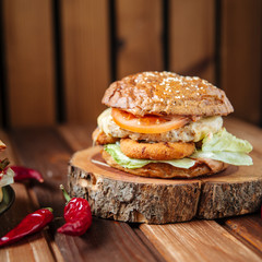 Delicious juicy hamburger, wooden brown background, hot peppers, vegetables, square, side view, closeup