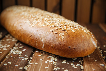 Delicious fresh dark loaf of bread on the wooden background, side view