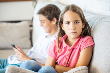 Happy boy playing on smartphone next to his angry sister looking at camera