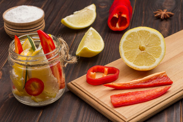 Fermented lemons with salt in jars and chili pepper on cutting board.